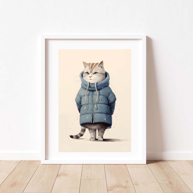 May include: A framed wall art print featuring a light gray tabby cat wearing a blue puffer jacket with a high collar and long drawstrings. The cat has dark stripes on its head and tail, standing against a solid light beige background.