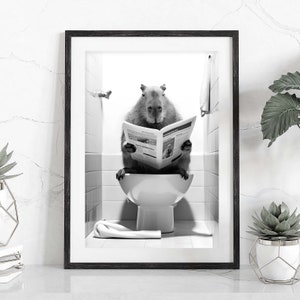 May include: A black and white photo of a capybara sitting on a toilet and reading a newspaper. The capybara is in a bathroom with white tile walls and a white toilet.