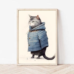 May include: A framed wall art print featuring a grey tabby cat standing upright and wearing a blue hooded jacket with horizontal stripes and two brown buttons. The cat has a serious expression and is depicted against a plain cream background.