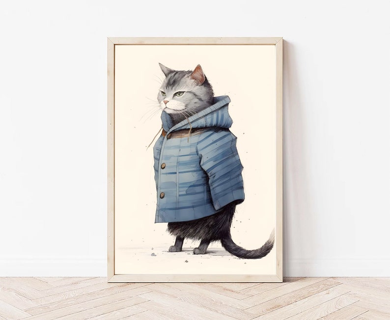 May include: A framed wall art print featuring a grey tabby cat standing upright and wearing a blue hooded jacket with horizontal stripes and two brown buttons. The cat has a serious expression and is depicted against a plain cream background.