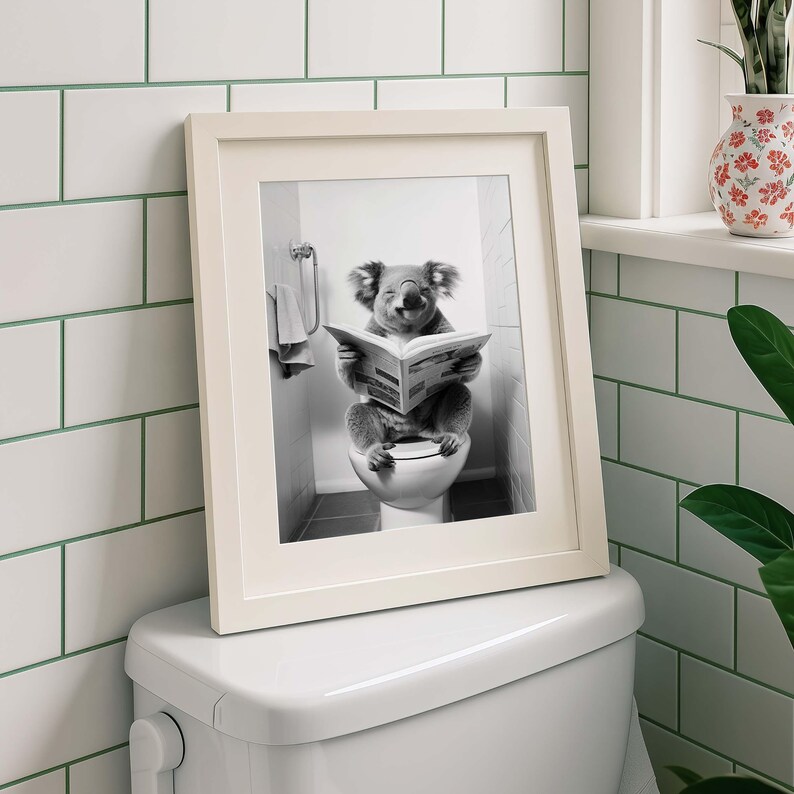 Puede incluir: Una impresi&oacute;n enmarcada en blanco y negro que muestra a un koala sentado en un inodoro blanco mientras lee un peri&oacute;dico abierto. El koala est&aacute; posicionado en el centro de la imagen, sosteniendo el papel con ambas patas, frente a una pared de azulejos.
