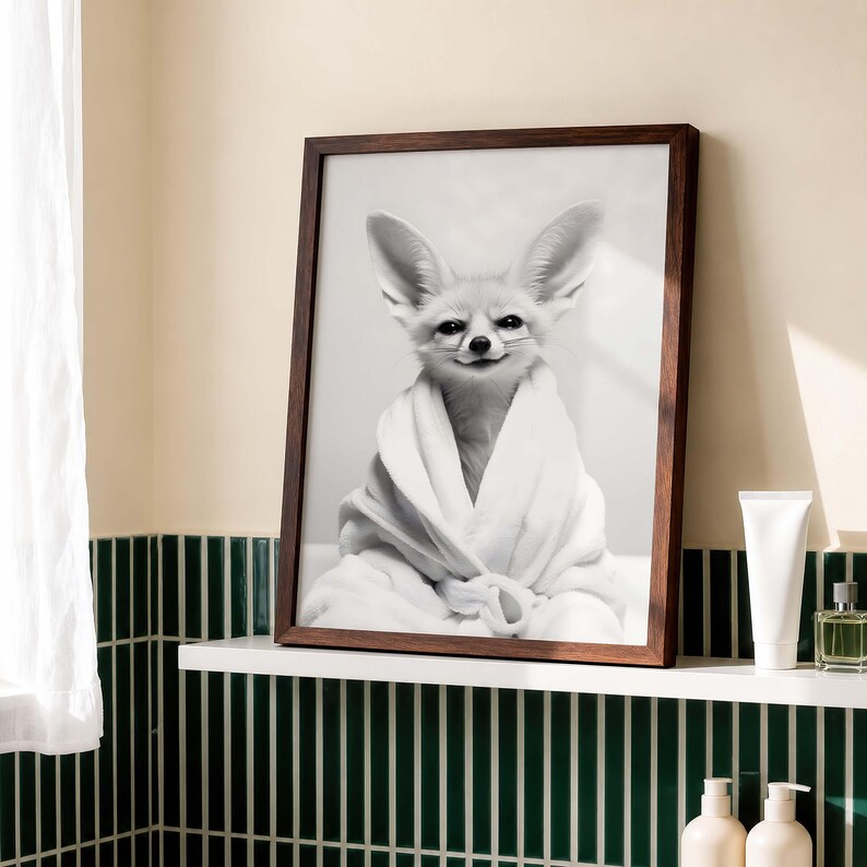K&ouml;nnte beinhalten: Ein gerahmter Schwarz-Wei&szlig;-Wandkunstdruck, der einen W&uuml;stenfuchs mit gro&szlig;en Ohren zeigt, der in einen flauschigen wei&szlig;en Bademantel geh&uuml;llt ist. Der Fuchs hat ein dezentes L&auml;cheln und ist in einem dunkelbraunen Holzrahmen zentriert.