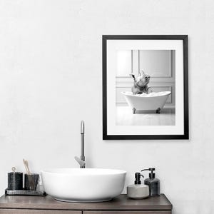 Pu&ograve; includere: Foto in bianco e nero di un rinoceronte che fa il bagno in una vasca da bagno bianca. Il rinoceronte &egrave; seduto nella vasca con la testa e il collo sopra l'acqua. La foto &egrave; incorniciata da una cornice nera.