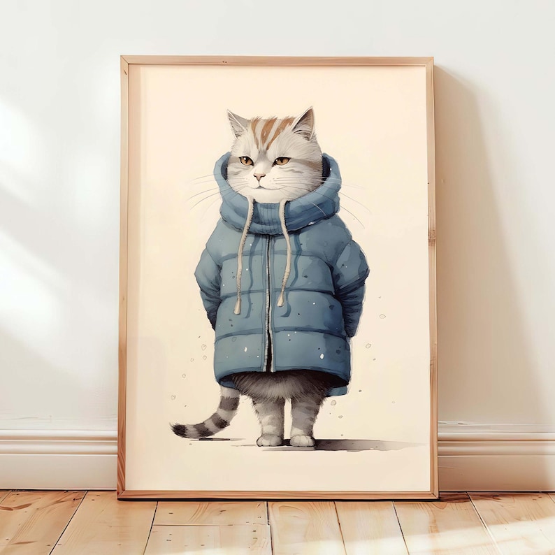 May include: A framed wall art print featuring a grey and white tabby cat wearing a blue puffer jacket with a high collar and drawstrings. The cat is standing upright, facing forward, with its tail visible on the left side against a cream background.