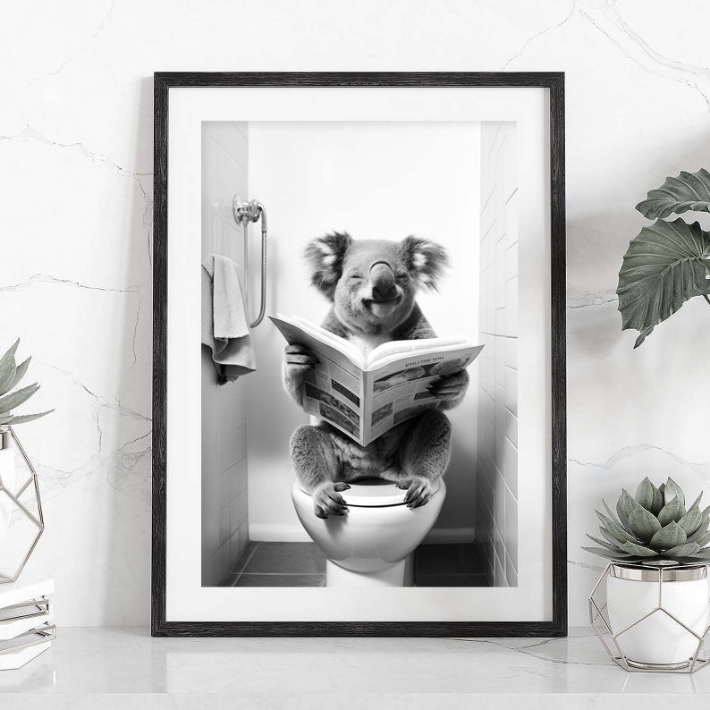 Puede incluir: Una impresi&oacute;n de arte mural enmarcada en blanco y negro que muestra a un koala sentado en un inodoro blanco mientras lee un peri&oacute;dico abierto. El koala tiene una expresi&oacute;n sonriente y est&aacute; en un ba&ntilde;o con azulejos y una toalla en la pared.