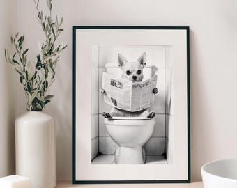 May include: A black and white framed wall art print featuring a small dog sitting on a white toilet while holding and reading an open newspaper. The scene is set against a tiled bathroom wall background, captured in a high-contrast monochrome style.