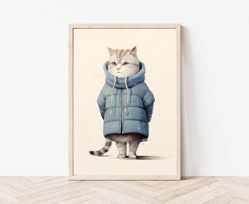 May include: A framed wall art print featuring a light-colored tabby cat wearing a blue puffer jacket with a high collar and drawstrings. The cat has grey and white fur with orange stripes on its head and a striped tail, standing against a cream background.