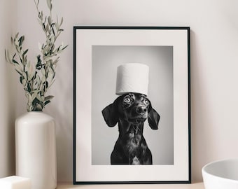 May include: A framed black and white wall art print featuring a portrait of a black dachshund dog with a roll of white toilet paper balanced on its head. The dog has large, expressive eyes looking upward toward the toilet paper roll.