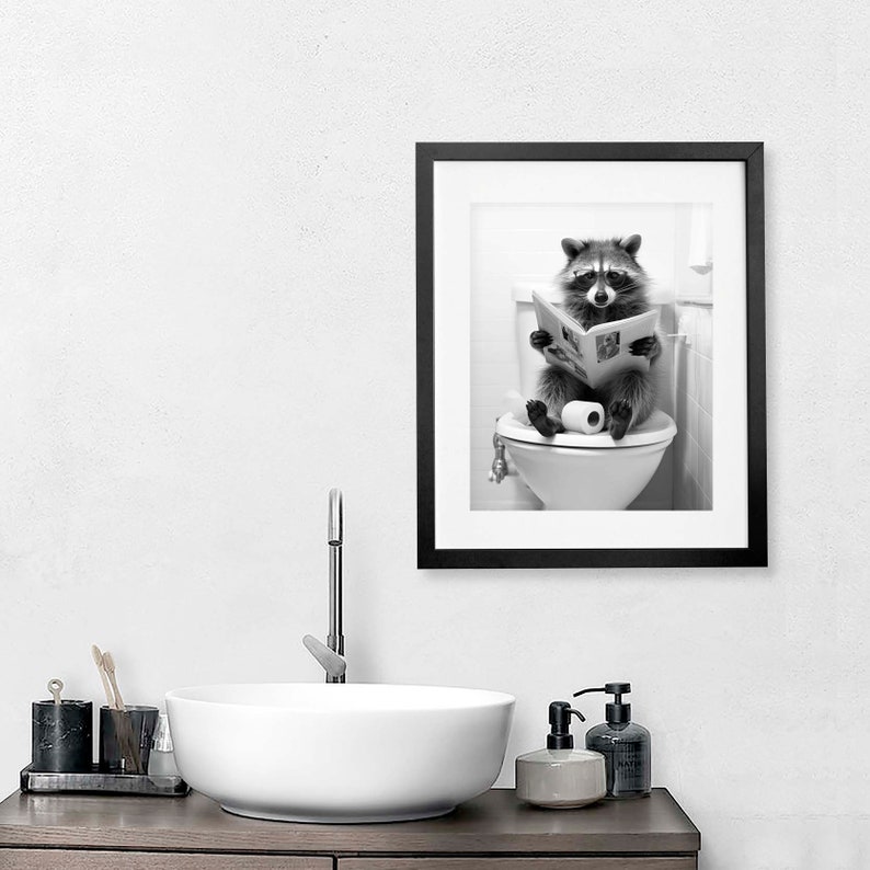 May include: A black and white framed wall art print featuring a raccoon sitting on a white toilet, holding an open newspaper in its paws. The raccoon is positioned centrally on the toilet seat with a roll of toilet paper resting beside its feet.