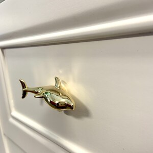 May include: Gold shark drawer pull. The shark is facing right and has a shiny finish.