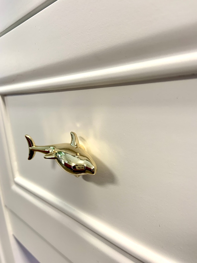 May include: Gold shark drawer pull. The shark is facing right and has a shiny finish.