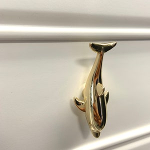 May include: Gold-toned dolphin shaped drawer pull. The dolphin is facing upwards with its tail in the air.