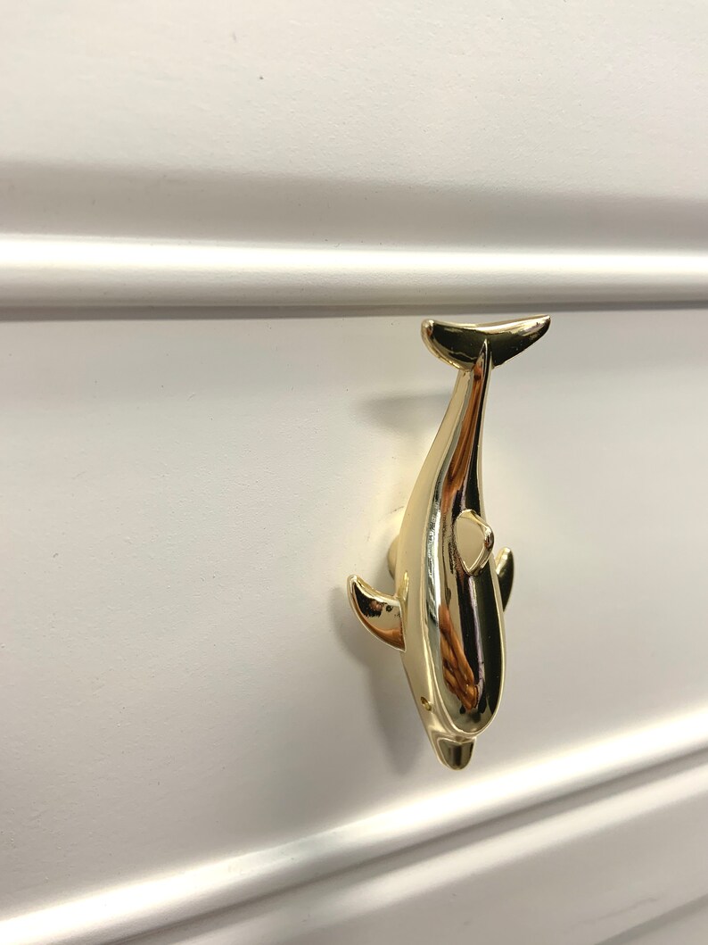 May include: Gold-toned dolphin shaped drawer pull. The dolphin is facing upwards with its tail in the air.