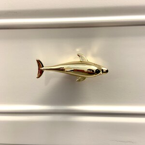 May include: Gold dolphin drawer pull. The dolphin is facing right and has a smooth, shiny finish.
