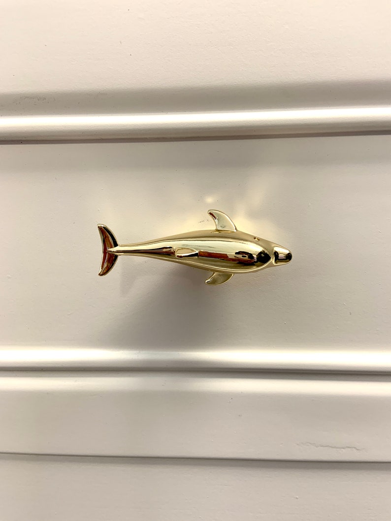 May include: Gold dolphin drawer pull. The dolphin is facing right and has a smooth, shiny finish.