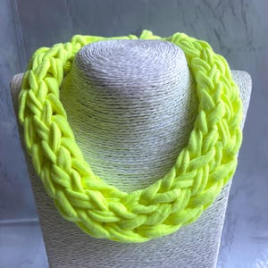 May include: A bright neon yellow braided necklace made from fabric. The necklace is displayed on a white mannequin.