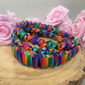 May include: A set of three colourful braided headbands. The headbands are made of woven fabric in a variety of bright colours, including red, orange, yellow, green, blue, and purple.