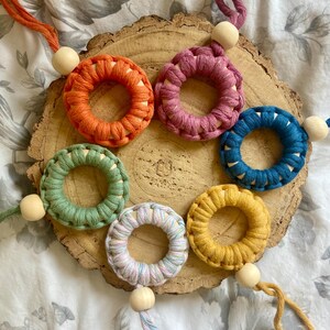 May include: Six crocheted rings with wooden beads, each ring is a different colour: orange, pink, blue, green, yellow, and multi-coloured.