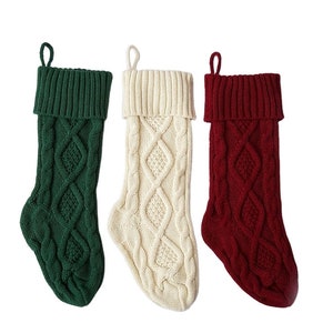 May include: Three knitted Christmas stockings in green, white, and red with a cable knit pattern.