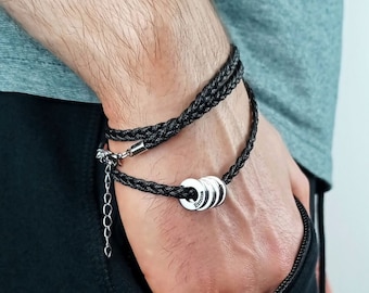 May include: A black braided bracelet with silver metal rings. The rings have the word "forever" engraved on them.