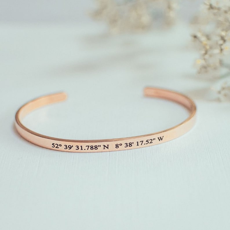 Puede incluir: Un brazalete de oro rosa con las coordenadas "52&deg; 39' 31.788" N 8&deg; 38' 17.52" W" grabadas.