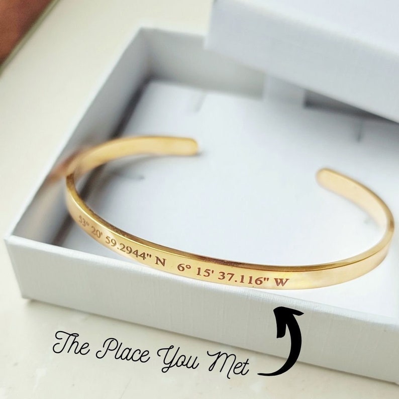 Puede incluir: Un brazalete de oro con las coordenadas "53&deg; 20' 59.2944" N 6&deg; 15' 37.116" W" grabadas en &eacute;l. El texto "The Place You Met" est&aacute; escrito debajo del brazalete.