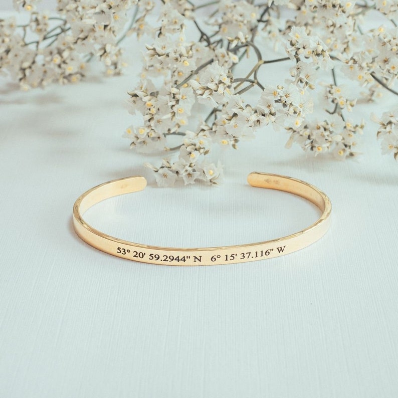 Puede incluir: Pulsera de brazalete de tono dorado con acabado martillado. La pulsera est&aacute; grabada con las coordenadas "53&deg; 20' 59.2944" N 6&deg; 15' 37.116" W".