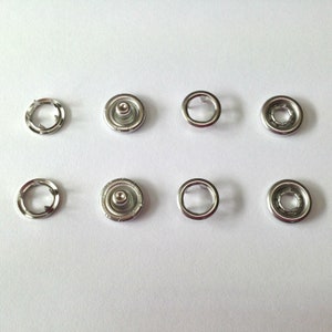 May include: A set of silver metal snap fasteners, also known as poppers, for clothing or crafts. The set includes both male and female fasteners.