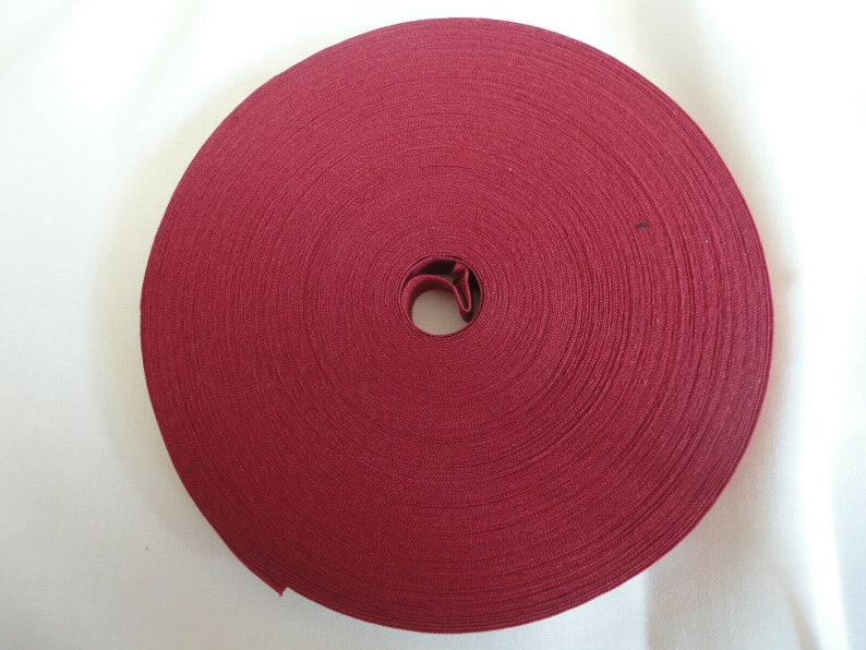 Puede incluir: Un rollo de ribete de tela color burdeos, enrollado en un c&iacute;rculo.