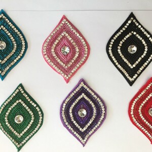 May include: Six diamond-shaped fabric patches with a central rhinestone and a beaded border. The patches are in teal, pink, black, green, purple, and red.