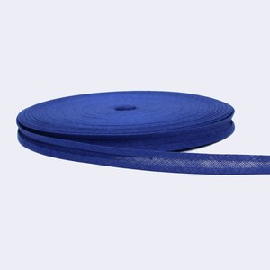 Puede incluir: Un rollo de cinta de bies azul, un tipo de adorno de tela que se utiliza para terminar los bordes de la tela.