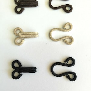 May include: Six toggle clasps in three colours: brown, beige, and black. Each clasp has a loop on one end and a double loop on the other end.
