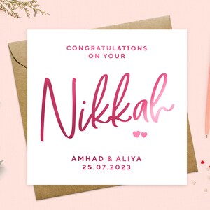 May include: White card with pink calligraphy that says "Congratulations on your Nikkah" with two pink hearts below. The card also says "Ahmad & Aliya 25.07.2023".