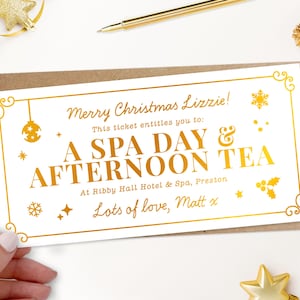 May include: A gold-colored gift certificate with the text "Merry Christmas Lizzie!" and "A SPA DAY & AFTERNOON TEA." The certificate is decorated with festive ornaments and is on a white background.