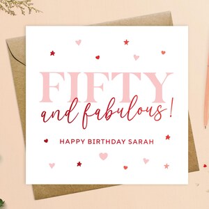 May include: A white card with pink and red hearts and stars. The text on the card reads "Fifty and fabulous! Happy Birthday Sarah".