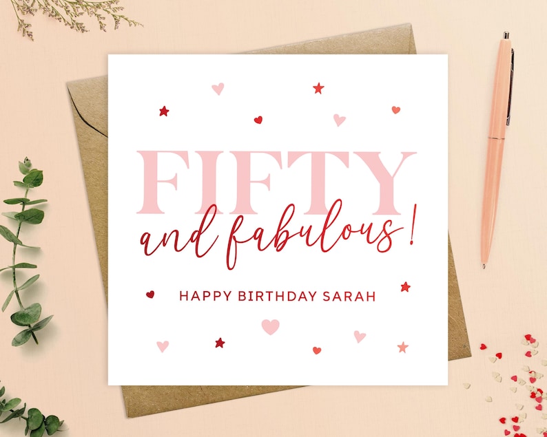 May include: A white card with pink and red hearts and stars. The text on the card reads "Fifty and fabulous! Happy Birthday Sarah".