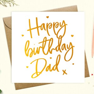 May include: A white card with gold foil lettering that says "Happy birthday Dad" with a small gold cross at the end of the text.