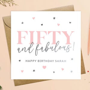 May include: A white card with pink and gray text and hearts and stars. The text reads "FIFTY and fabulous! Happy Birthday Sarah".