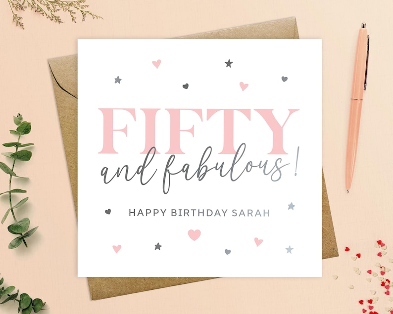 May include: A white card with pink and gray text and hearts and stars. The text reads "FIFTY and fabulous! Happy Birthday Sarah".