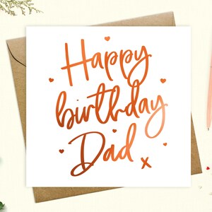 May include: A white card with a copper foil inscription that reads "Happy birthday Dad" with small hearts scattered around the text.