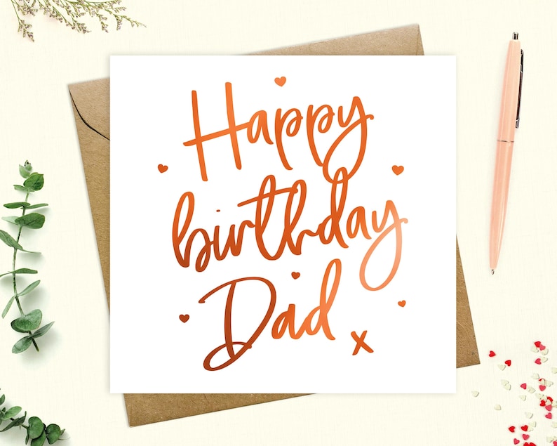 May include: A white card with a copper foil inscription that reads "Happy birthday Dad" with small hearts scattered around the text.