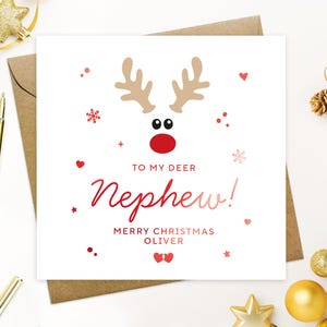 May include: A square white Christmas card with a reindeer design and the text "TO MY DEER Nephew!" in red. The card includes the message "MERRY CHRISTMAS OLIVER" and is decorated with hearts and snowflakes.