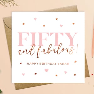 May include: A white card with pink and copper foil accents. The card says "Fifty and fabulous!" with the name "Sarah" in copper foil. The card is decorated with pink hearts and copper stars.