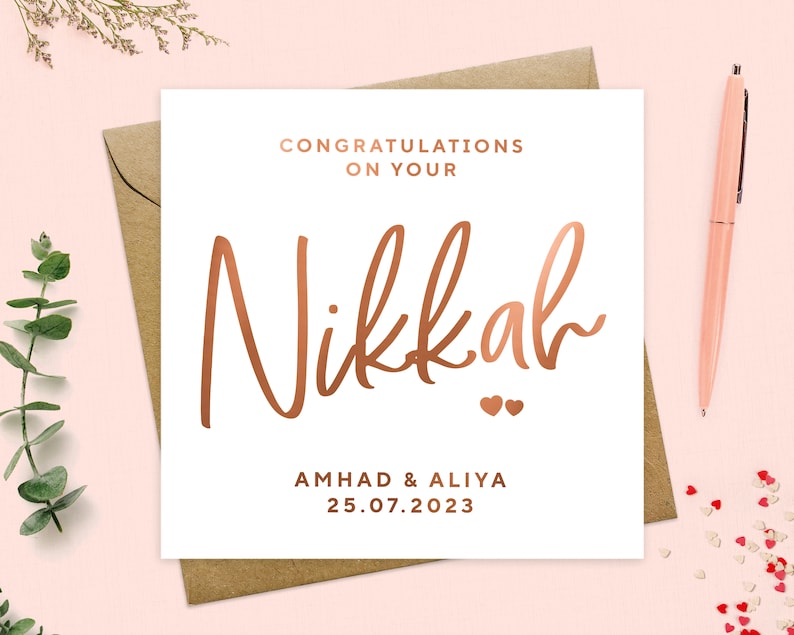 May include: A white card with a rose gold inscription that reads "Congratulations on your Nikkah" with two small hearts below the text. The names Ahmad & Aliya and the date 25.07.2023 are also written in rose gold below the hearts.