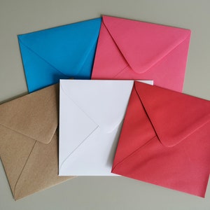 May include: Five envelopes in different colors: brown, white, blue, pink, and red. The envelopes are all the same size and shape, and they are arranged in a semi-circle.