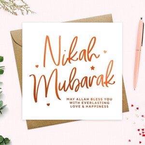 May include: A white card with the words "Nikah Mubarak" written in copper foil lettering. The card also includes the text "May Allah bless you with everlasting love & happiness".