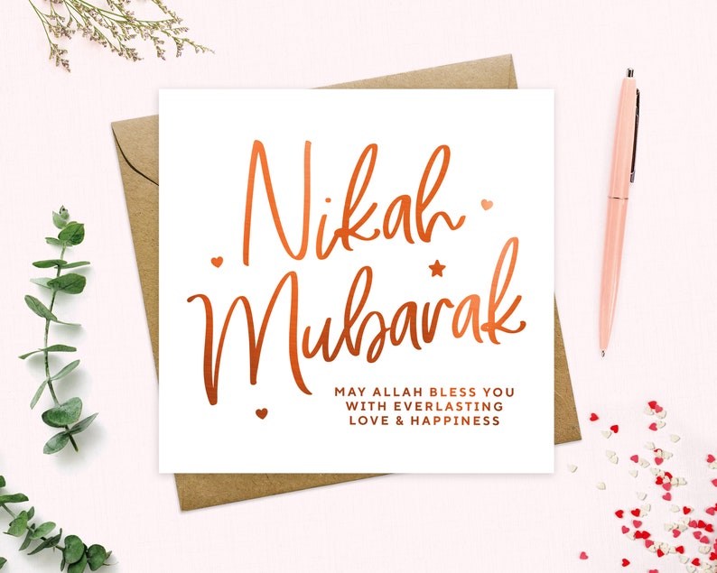 May include: A white card with the words "Nikah Mubarak" written in copper foil lettering. The card also includes the text "May Allah bless you with everlasting love & happiness".