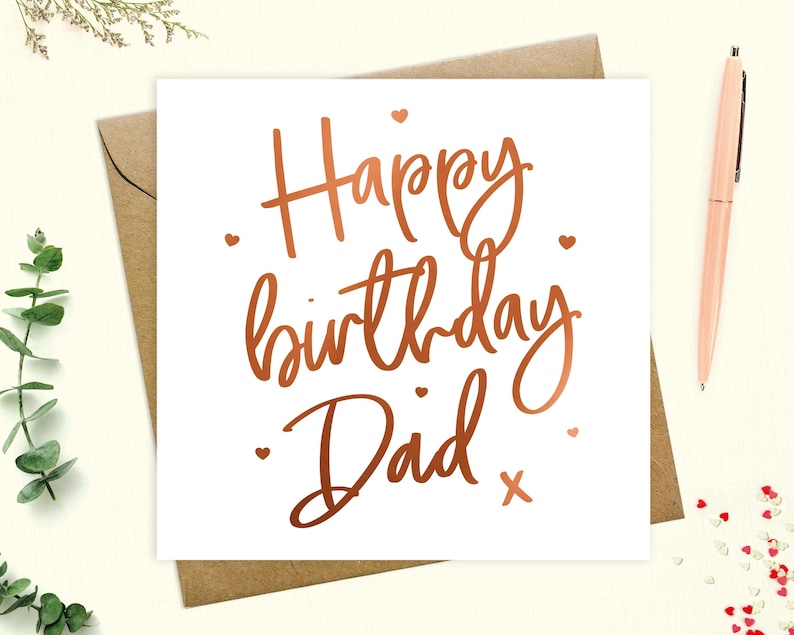 May include: A white card with a copper foil inscription that reads "Happy birthday Dad" with a small copper foil cross at the end of the inscription. There are small copper foil hearts scattered around the inscription.