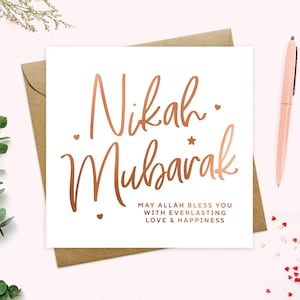 May include: A white card with a rose gold foil inscription that reads "Nikah Mubarak" and "May Allah bless you with everlasting love & happiness".
