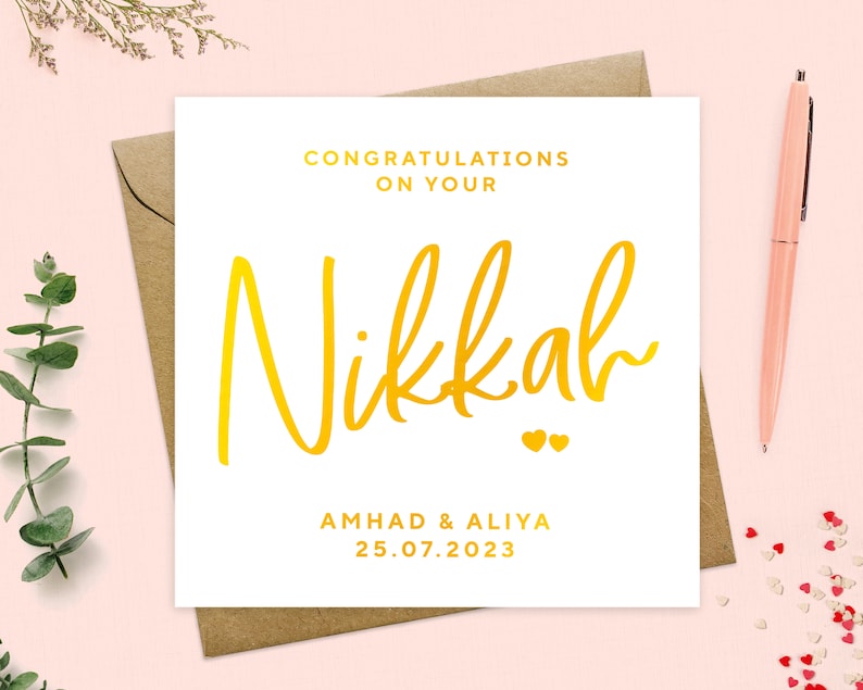 May include: White card with gold lettering announcing a Nikkah for Amhad & Aliya on 25.07.2023. The word Nikkah is written in a large, stylized font.
